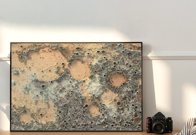 May include: A framed abstract print of a beige and gray textured surface with a pattern of craters. The print is in a black frame.