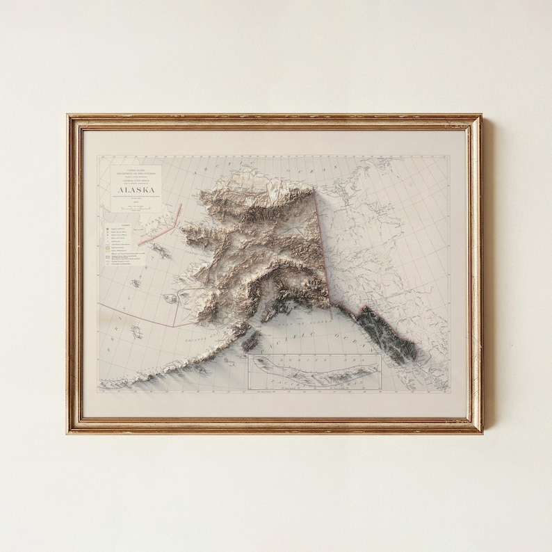 May include: Framed 3D relief map of Alaska, showcasing the state's topography in shades of brown and white. The map is set against a vintage-style background with geographical details and is encased in a gold-colored frame.