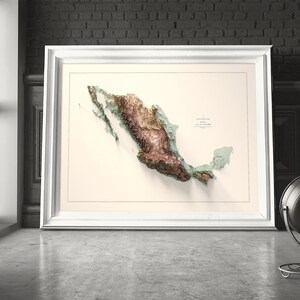 May include: A framed 3D relief map of Mexico, showcasing the country's topography in shades of brown, green, and beige. The map is set against a neutral background and framed in white. The artwork is displayed on a concrete floor.