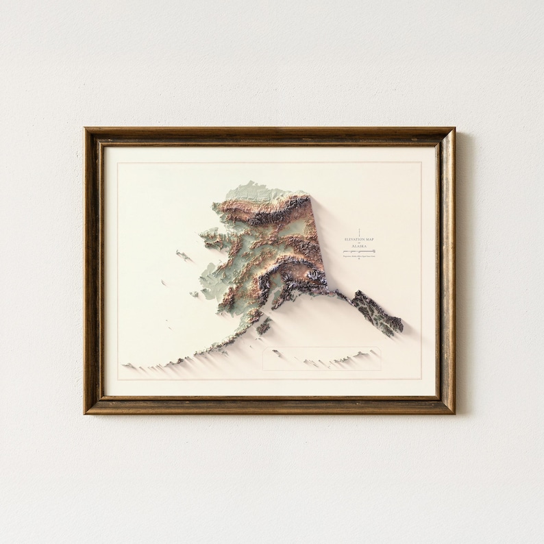 May include: Framed 3D elevation map of Alaska, showcasing the state's topography in shades of brown, green, and white. The map is set against a cream-colored background and enclosed in a brown wooden frame.