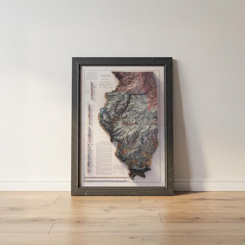 May include: Framed 3D map of Illinois, showcasing the state's topography with detailed relief. The map features a color palette of greens, browns, and purples, set within a dark gray wooden frame. The map is displayed on a white wall.