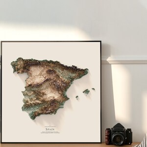 Pode incluir: Um mapa topogr&aacute;fico da Espanha com um efeito 3D, mostrando o terreno variado do pa&iacute;s em tons de verde, marrom e bege. O mapa est&aacute; emoldurado e exibido contra uma parede branca.