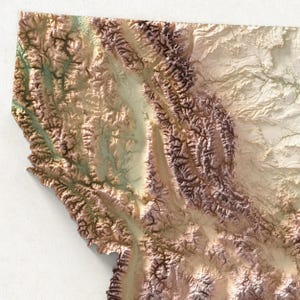 May include: A detailed relief map of Montana, USA, showcasing the state's mountainous terrain. The map features a 3D effect with varying shades of brown, tan, and green, highlighting the valleys and peaks. The map is a close-up view, with the state's outline visible.