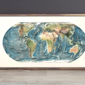 May include: A rectangular framed wall art piece featuring an oval-shaped world map with detailed topographical relief. The map displays continents in shades of green and brown, surrounded by deep blue oceans, all encased in a simple wooden frame.