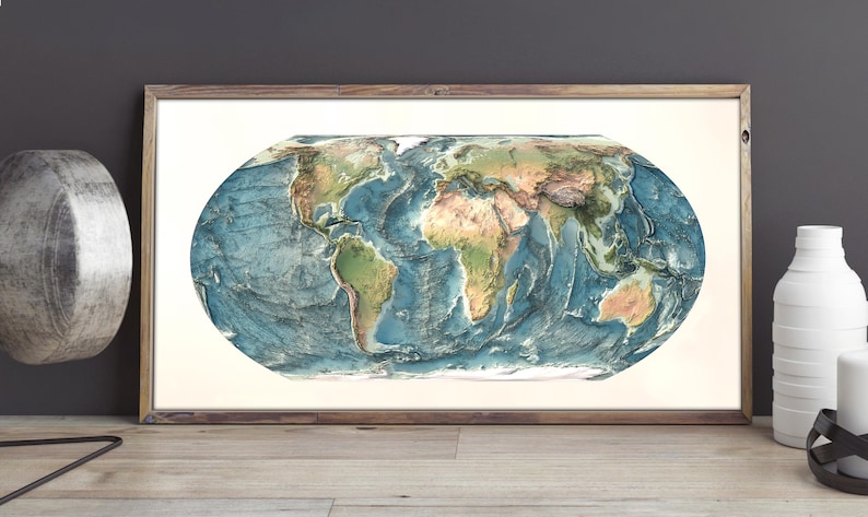 May include: A rectangular framed wall art piece featuring an oval-shaped world map with detailed topographical relief. The map displays continents in shades of green and brown, surrounded by deep blue oceans, all encased in a simple wooden frame.