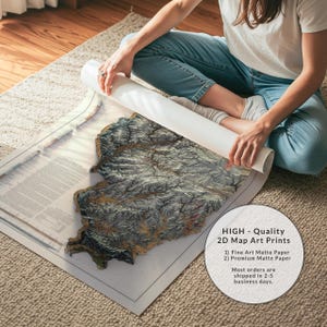 May include: A detailed 2D map art print with a textured, topographic design. The map is primarily gray and brown, with a white border. The print is being unrolled, revealing the intricate details of the artwork. The image includes text that says "HIGH - Quality 2D Map Art Prints".