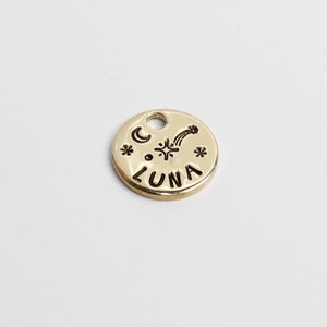 May include: Gold-colored metal charm with the word "LUNA" and a crescent moon, star, and shooting star design.