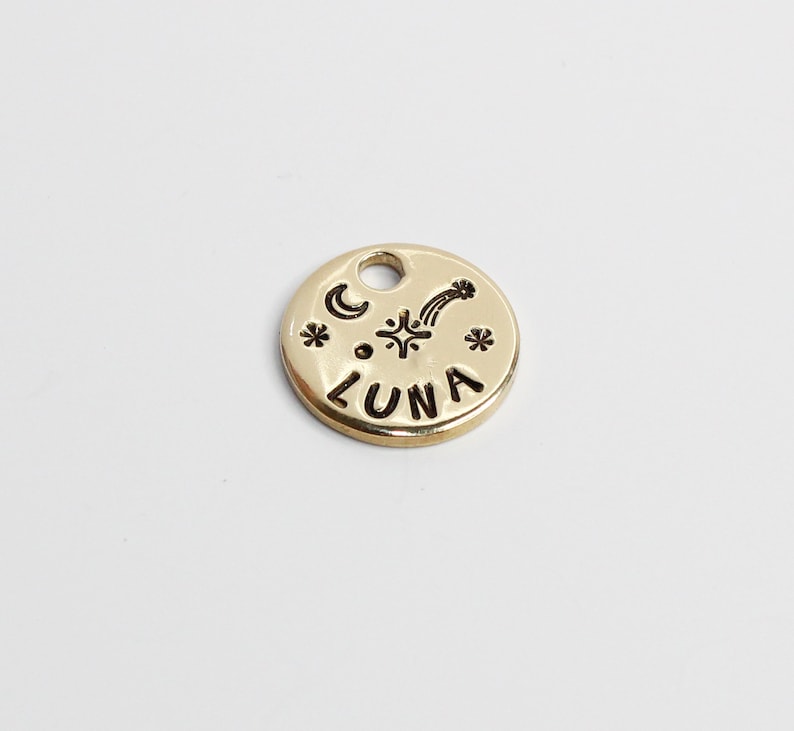 May include: Gold-colored metal charm with the word "LUNA" and a crescent moon, star, and shooting star design.