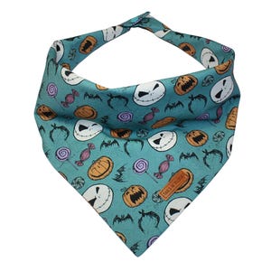 May include: Teal blue bandana with a repeating pattern of Jack Skellington's face, pumpkins, bats, and candy. The bandana has a brown leather tag with the text "Tails N' Tippers".