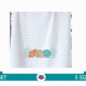 Puede incluir: Diseño bordado de tres conchas marinas con coral sobre una toalla blanca. Las conchas son de color naranja, marrón y blanco. El coral es turquesa.