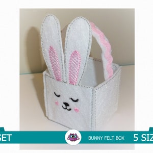 Pode incluir: Caixa de feltro branca em forma de coelho com orelhas cor-de-rosa e uma alça cor-de-rosa. A caixa tem um rosto de coelho bordado bonito. O texto "1 SET" e "BUNNY FELT BOX" são visíveis na imagem. O texto "5 SIZES" também é visível na imagem.