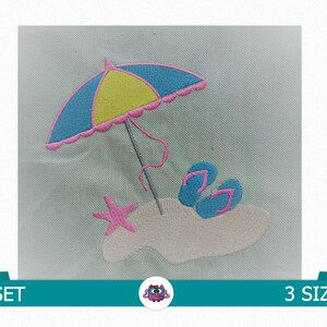 Op de afbeelding: Borduurwerk van een strandsc&egrave;ne met een blauwe en gele parasol, roze slippers en een roze zeester op een wit zandstrand.