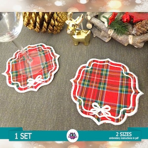 Pode incluir: Dois  copos de tecido xadrez vermelho e verde com bordas brancas festoneadas e um laço branco no centro. Os copos estão sobre uma superfície marrom. 1 CONJUNTO, 2 TAMANHOS, instruções de bordado em pdf.