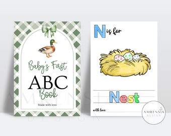 May include: A two-page spread from a baby's ABC book. The left page features a duck illustration and the text "Baby's First ABC Book." The right page shows a nest with eggs and the word "Nest."