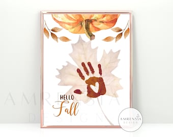 Può includere: Una stampa d'arte stampabile con un'illustrazione ad acquerello di un'impronta di mano su una foglia con il testo "Hello Fall". La stampa presenta una tavolozza di colori autunnali arancio, marrone e giallo.