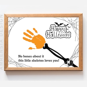 May include: A white framed print with a black spiderweb design. The print features an orange handprint with a black skeleton arm extending from it. The text "Happy Halloween!" is in black lettering. The text "No bones about it this little skeleton loves you!" is also in black lettering.