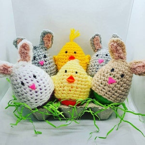 May include: Five crocheted Easter eggs in an egg carton. The eggs are decorated as a bunny, chick, and a mouse. The eggs are in a green egg carton with green grass.