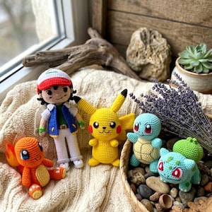 May include: A collection of four crocheted figures including a human character with a red and white cap, a yellow mouse-like creature with red cheeks, a light blue turtle, and a light green creature with a bulbous plant on its back.