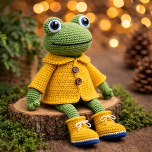 May include: A handmade crochet frog doll with a green body, large blue and white eyes, and a smiling mouth. It wears a yellow coat with brown buttons and matching yellow boots with white bows. The doll is sitting on a wooden slice.