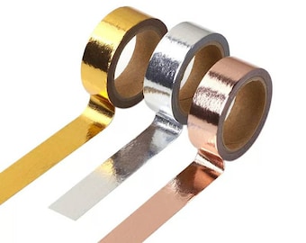 May include: Three rolls of metallic adhesive tape arranged in a diagonal row. The rolls feature a shiny, reflective finish in gold, silver, and rose gold colors, each wound around a brown cardboard core with a strip of tape extending outward.