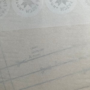 May include: A light-colored sewing pattern paper featuring repeating circular logos that read Creative Patch London. The paper includes printed lines, the text Doublure, and a small icon of scissors along a dashed cutting line for garment construction.