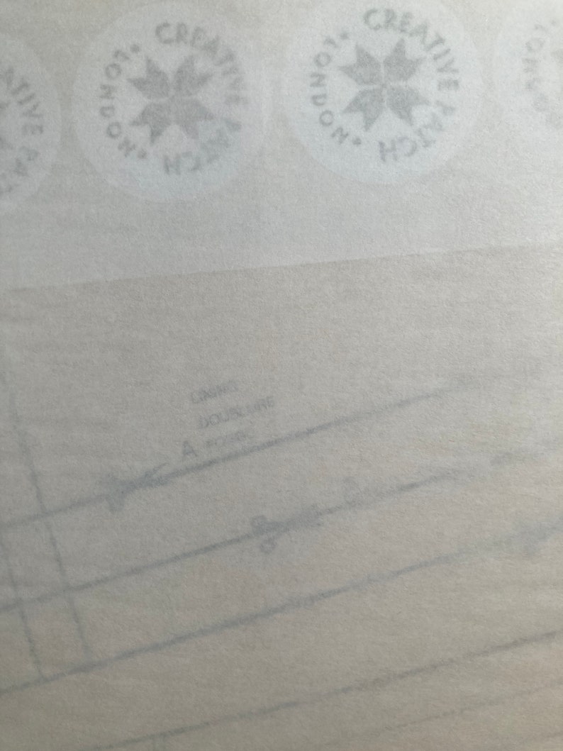 May include: A light-colored sewing pattern paper featuring repeating circular logos that read Creative Patch London. The paper includes printed lines, the text Doublure, and a small icon of scissors along a dashed cutting line for garment construction.