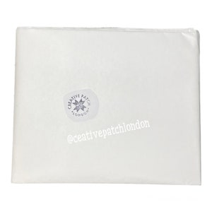 May include: A rectangular sheet of white tissue paper folded neatly. A circular sticker is affixed to the surface, featuring a star-like emblem and the text CREATIVE PATCH LONDON. The text @ceativepatchlondon is printed in white on the paper.