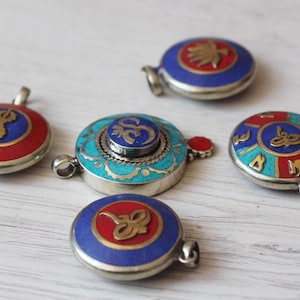 May include: Five round pendants with intricate designs. Each pendant features a different symbol, including a lotus flower, a mantra, and a stylized design. The pendants are made of silver and have a blue, red, and turquoise enamel finish.