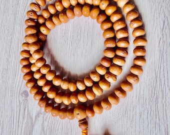 May include: A brown wooden mala bead necklace with a tassel. The beads are round and have a smooth finish. The tassel is made of a yellow cord.