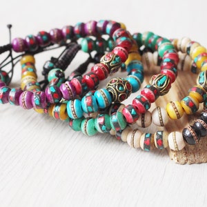 May include: Five colorful beaded bracelets with intricate designs and metal accents. The bracelets are stacked on a wooden surface.