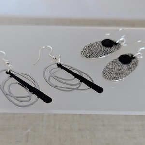 May include: Silver-tone and black earrings. Two pairs of earrings are displayed. One pair features a black oval with a silver-tone wire design. The other pair has a black oval with a silver-tone mesh design. Both pairs have silver-tone ear wires.