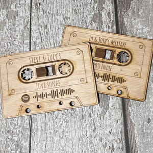 May include: Two wooden cassette tape-shaped plaques with personalised text and Spotify barcodes. The top plaque reads "Jo & Josh's Mixtape" and "90's Indie". The bottom plaque reads "Steve & Lucy's" and "Love Songs".