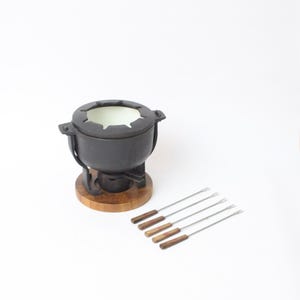 Può includere: Una pentola per fonduta nera con base in legno e un set di forchette per fonduta. La pentola ha un interno bianco e un manico su ogni lato. Le forchette hanno manici in legno e rebbi in acciaio inossidabile. Un set classico per l'intrattenimento.