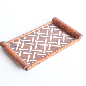 May include: Rectangular wooden tray with a woven pattern in brown and white. The tray has rolled edges on both ends. The tray is likely used for serving food or displaying items. The tray is on a white background.