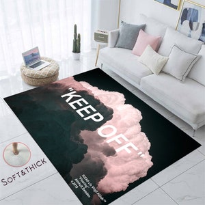Può includere: Un tappeto nero e rosa con una sovrapposizione di testo bianco "KEEP OFF". Il tappeto presenta un design a nuvole con una texture morbida e spessa.