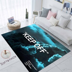 Può includere: Un tappeto blu e nero con un design a nuvole bianche e il testo "KEEP OFF" stampato su di esso. Il tappeto ha una texture morbida e spessa.