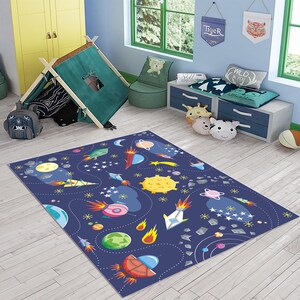 May include: A blue and white space-themed rug with rockets, planets, stars, and comets. The rug is on a wooden floor in a room with a play tent, a chair, and a bookshelf.
