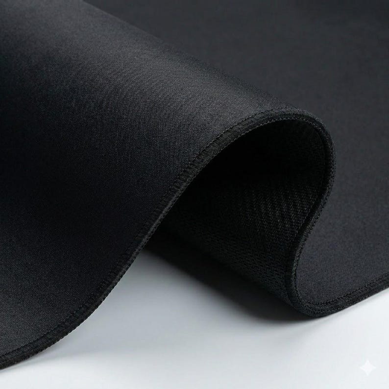 K&ouml;nnte beinhalten: Nahaufnahme eines schwarzen Stoffes mit glatter, gewebter Textur. Der Stoff ist gefaltet und zeigt eine kontrastierende, strukturierte Unterseite und gen&auml;hte Kanten. Das Bild hebt die Tiefe und die Details des Materials hervor.