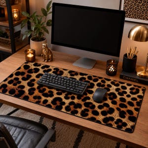 Può includere: Tappetino da scrivania rettangolare con stampa leopardata. Il tappetino presenta un motivo di macchie marroni e nere su sfondo beige. Una tastiera e un mouse neri sono sul tappetino, insieme a un monitor del computer.