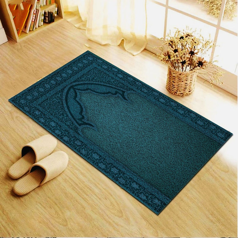 May include: A teal blue prayer rug with a decorative border and a central arch design. The rug is on a wooden floor.