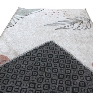 May include: A beige rug with a geometric pattern and a black and white geometric pattern on the back. The rug has a floral design with brown and green accents.