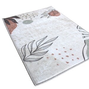 May include: A beige area rug with a modern abstract design featuring brown, green, and black leaves and shapes.