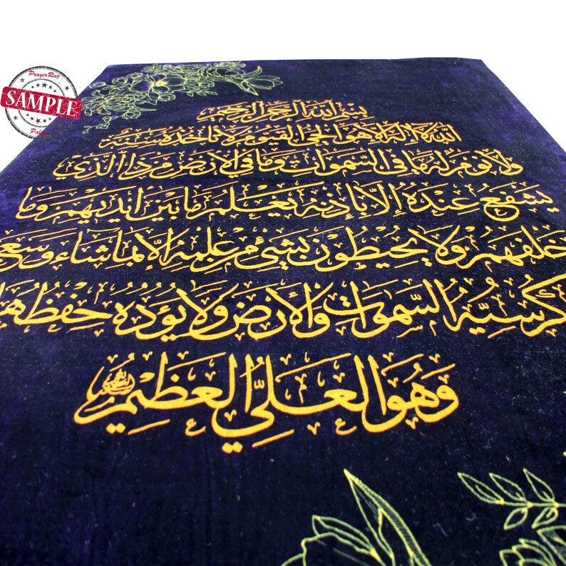 May include: A dark blue prayer rug with gold Arabic calligraphy. The rug features intricate floral designs in the corners and edges. The text is a prominent feature, covering most of the rug's surface.