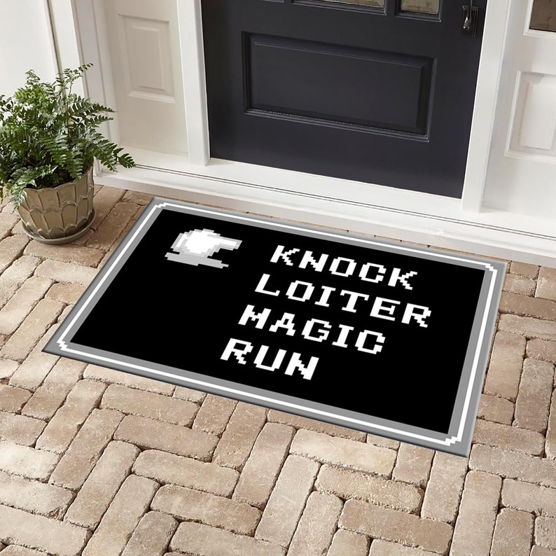 May include: Black doormat with white text that reads "Knock Loiter Magic Run" in a pixelated font. The doormat has a grey border.