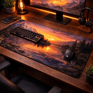 Könnte beinhalten: Ein großes rechteckiges Mauspad mit einem malerischen Sonnenuntergang über einem See und Bergen. Eine schwarze Tastatur und Maus befinden sich auf dem Pad. Das Pad liegt auf einem Holzschreibtisch mit Monitor, Kopfhörern und einer Lampe.