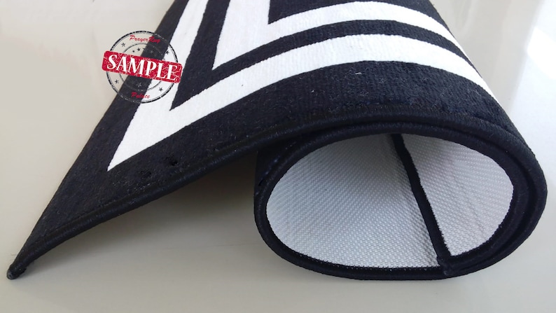 May include: A black and white geometric patterned rug rolled up, showing the black backing and white woven fabric.