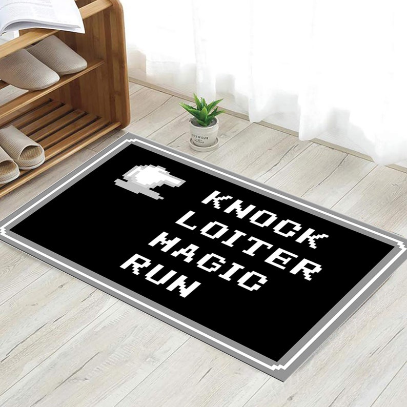 May include: Black and white rug with a grey border. The rug features a pixelated spaceship and the words "Knock Loiter Magic Run" in white.
