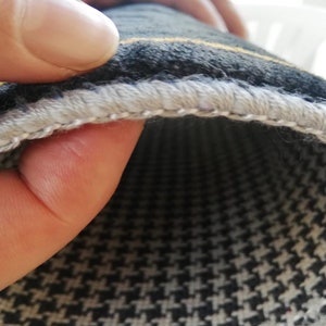 May include: Close-up of the edge of a black and white patterned rug with a gray and yellow trim. The rug has a houndstooth pattern.