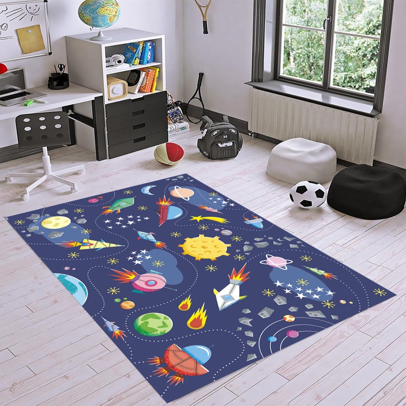 May include: A blue and white space-themed rug with rockets, planets, stars, and comets. The rug is on a light wood floor.