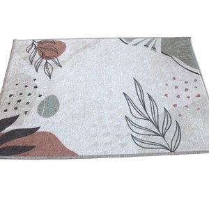 May include: A beige rug with a modern abstract design featuring brown, green, and black leaves and shapes.